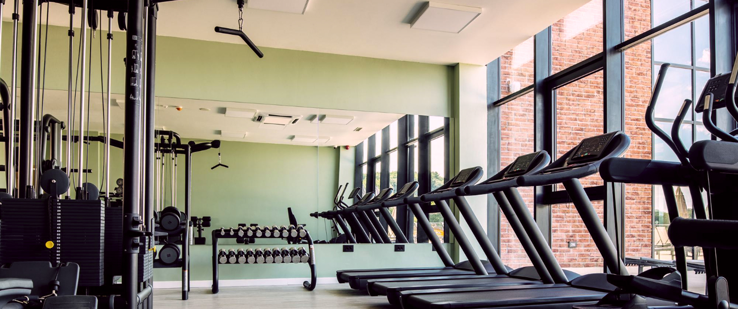 Тренажерный зал с огромным зеркалом на стене, беговыми дорожками, набором гантель и панорамными окнами